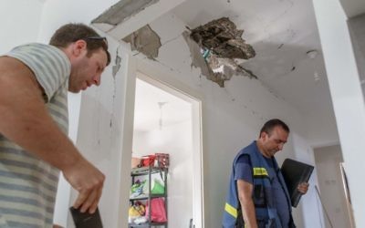 Des travailleurs de l'autorité fiscale évaluent les dommages causés à une maison après avoir été touchée par une roquette au Conseil régional Hof Ashkelon le 20 août, 2014 (Crédit : Flash90)