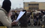 Un combattant de l'Etat islamique lisant les charges contre deux personnes crucifiées (en arrière plan) (Crédit : Capture d'écran)