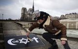 Un homme collant une affiche 'Coexist' de COMBO le 8 février 2015 sur le quai de la Tournelle, près de l'Institut du monde arabe. (Crédit : Joel Saget/AFP)