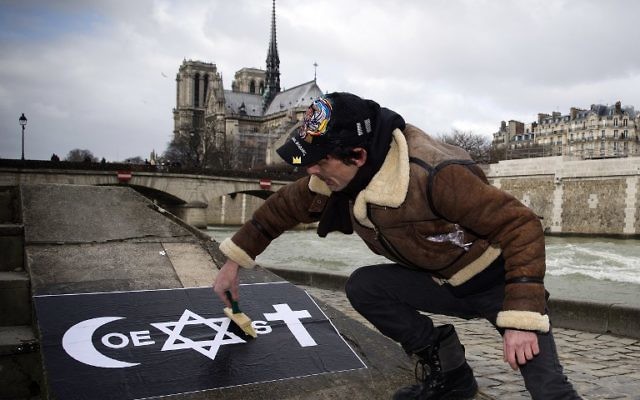 Un homme collant une affiche 'Coexist' de COMBO le 8 février 2015 sur le quai de la Tournelle, près de l'Institut du monde arabe. (Crédit : Joel Saget/AFP)