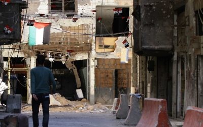 Une photo prise le 23 juin 2014 d'un homme marchant près d'un bâtiment criblé de balle dans le camp de réfugiés palestiniens de Yarmouk à Damas (Crédit : AFP PHOTO / LOUAI BESHARA)