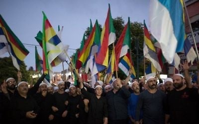 Les Druzes israéliens agitant des drapeaux lors d'une manifestation de quelque deux mille personnes dans  la ville druze de Daliyat al-Carmel, en Israël, appelant le gouvernement israélien à soutenir et à aider leurs frères de Syrie, le 14 juin 2015. (Crédit : AFP / MENAHEM KAHANA)