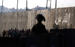 Un soldat de Tsahal observe des Palestiniens qui traversent le poste de contrôle de Qalandiya près de la ville de Ramallah en Cisjordanie (Crédit : Issam Rimawi / Flash90)