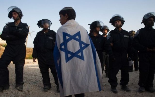 Un jeune garçon juif enveloppé du drapeau israélien face aux forces de sécurité israéliennes qui venaient évacuer les constructions illégales dans l'implantation juive de Beit El, le 28 juillet 2015 (Crédit photo:Nati Shohat / Flash90)