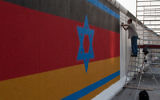 La fresque murale du mur de Berlin, peint à l'origine en 1988 par Günther Schaefer pour le 40e anniversaire de la Nuit de cristal en Allemagne nazie. La fresque est composée d'un drapeau israélien superposé sur un drapeau allemand (Crédit : CC-BY-SA Maartmeester/Flickr)