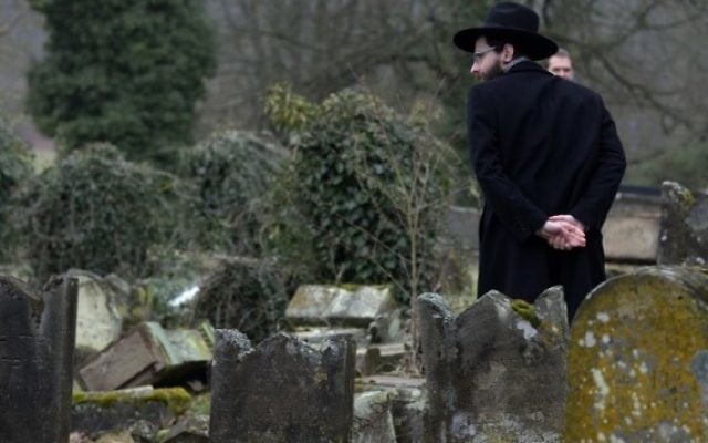Un membre de la communauté juive devant les pierres tombales brisées après la profanation de quelque 250 tombes, suite à  une cérémonie au cimetière juif de Sarre-Union, à l'est de la France, le 17 février 2015. (Crédit : Patrick Hertzog/AFP)