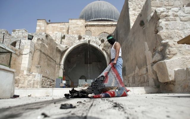 Un Palestinien masqué portant un bandeau du Hamas sort un tapis brûlé de la mosquée Al-Aqsa dans la Vieille Ville de Jérusalem lors des affrontements dans l'enceinte le 13 septembre 2015, quelques heures avant le début de la nouvelle année juive (Crédit : AFP PHOTO / AHMAD GHARABLI)