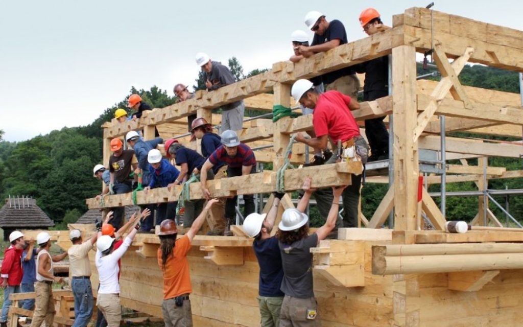 A Sanok en Pologne, les encadreurs et les étudiants ébéniste au niveau du sol à l'aide du travail d'équipe et de la puissance humaine collective pour soulever une poutre finie sur la structure du toit (Crédit : Trillium Studios production)
