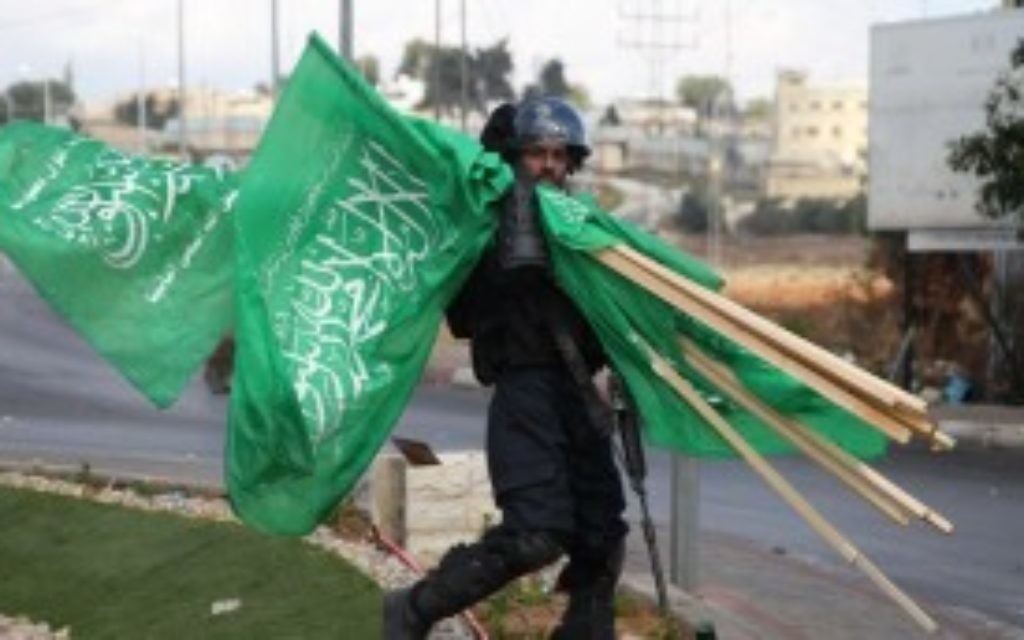 Un membre des forces de sécurité israéliennes porte  des drapeaux de l'organisation terroriste du Hamas qui ont été saisis lors d'affrontements avec des manifestants palestiniens près de limplantation de Beit El en Cisjordanie, le 8 octobre 2015 (Credit photo: Abbas Momani / AFP)