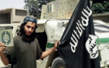 Abdelhamid Abaaoud, le cerveau présumé des attentats terroristes du 13 novembre à Paris, tenant un drapeau de l'Etat islamique dans cette image non datée d'un magazine publié par le groupe terroriste (Crédit : Capture d'écran)