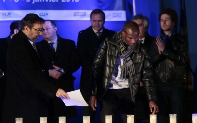 Lassana Bathily allume des bougies le 9 Janvier, 2016 près de l'Hyper Cacher,  lors d'une cérémonie organisée pour rendre hommage aux victimes de l'attentat contre le supermarché le 9 Janvier 2015 (Crédit : AFP / JACQUES DEMARTHON)