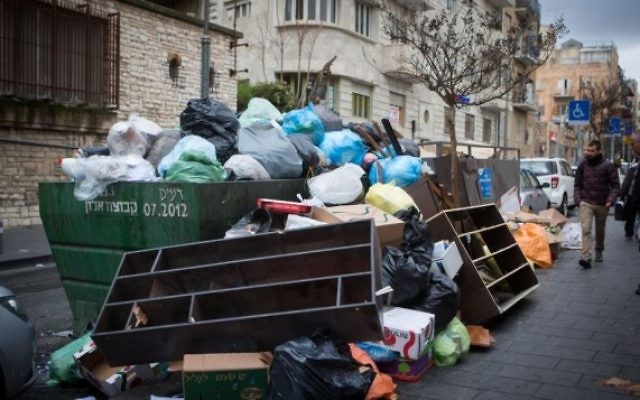 Un homme marche près d'un tas d'ordures dans le centre de Jérusalem, le 31 décembre 2015. (Crédit : Miriam Alster/ Flash90)