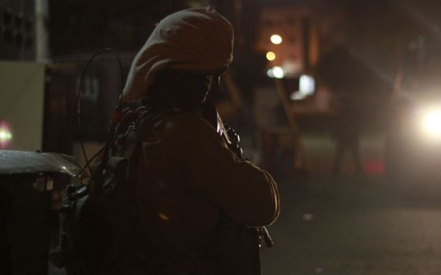 Un soldat de garde sous la lumière de la jeep de l'armée à Qalqilya le 14 janvier 2016. Les véhicules que l'armée utilise pendant ces raids nocturnes sont tous blindés contre les balles, les pierres et les cocktails Molotov. (Crédit : Judah Ari Gross/Times of Israel) Un soldat de garde sous la lumière de la jeep de l'armée à Qalqilya le 14 janvier 2016. Les véhicules que l'armée utilise pendant ces raids nocturnes sont tous blindés contre les balles, les pierres et les cocktails Molotov. (Crédit : Judah Ari Gross/Times of Israel)