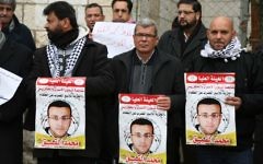Des militants palestiniens avec des affiches pendant une manifestation pour la libération du journaliste palestinien Mohammed al-Qiq devant le siège de la Croix rouge de Ramallah, en Cisjordanie, le 27 janvier 2016. (Crédit : Flash90)