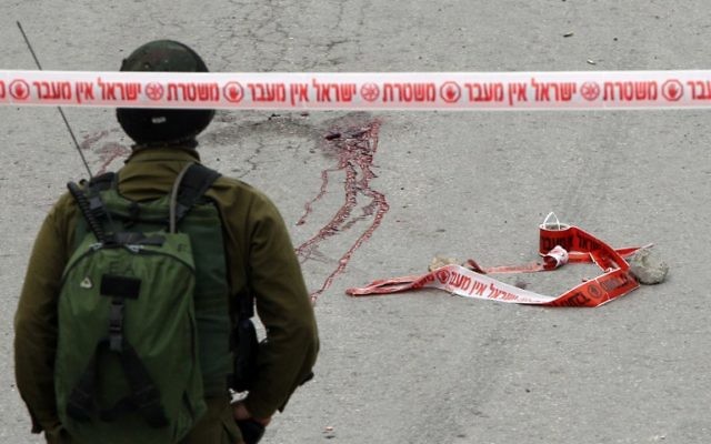Un soldat de Tsahal se tient près des taches d'un Palestinien qui aurait reçu une balle dans la tête tirée par un soldat alors qu'il gisait blessé sur le sol après avoir poignardé et blessé un soldat israélien à Hébron le 24 mars 2016 (Crédit : AFP / Hazem Bader) Un soldat de Tsahal se tient près des taches d'un Palestinien qui aurait reçu une balle dans la tête tirée par un soldat alors qu'il gisait blessé sur le sol après avoir poignardé et blessé un soldat israélien à Hébron le 24 mars 2016 (Crédit : AFP / Hazem Bader)