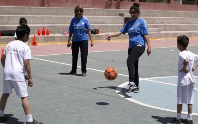 Des professeurs d'éducation physique palestiniennes (en bleu) et des enfants participent à une session d'entraînement organisée par la Fondation du Real Madrid dans une école de l'ONU du camp de réfugiés de Qalandiya, en Cisjordanie, le 25 avril 2016. (Crédit : AFP/ABBAS MOMANI) Des professeurs d'éducation physique palestiniennes (en bleu) et des enfants participent à une session d'entraînement organisée par la Fondation du Real Madrid dans une école de l'ONU du camp de réfugiés de Qalandiya, en Cisjordanie, le 25 avril 2016. (Crédit : AFP/ABBAS MOMANI)