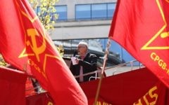 Jeremy Corbyn (au centre), chef du parti d'opposition britannique, le Parti travailliste, pendant un discours donné pendant un rassemblement du 1er mai depuis le toit d'un bus à deux étages entre des drapeaux du Parti communiste (marxiste-léniniste) anglais à Londres, le 1er mai 2016. (Crédit : AFP/JUSTIN TALLIS)