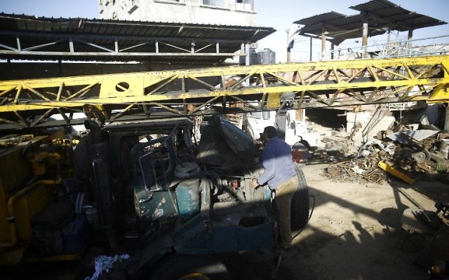 Un Palestinien inspecte un véhicule endommagé dans son atelier suite à des frappes par les forces aériennes israéliennes, à Gaza Ville, le 5 mai 2016 au matin.(Crédit : AFP/MOHAMMED ABED)