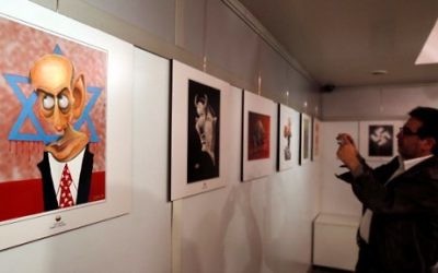 Un Iranien prend en photo un dessin exposé au concours international de caricatures sur l'Holocauste à Téhéran, le 14 mai 2016. (Crédit : AFP PHOTO / ATTA KENARE)