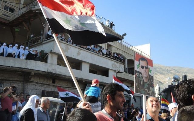 Un homme porte un drapeau syrien et un poster du présidet Bashar Al Assad au cours d'une manifestation pro armée syrienne, à Majdal Shams, lundi (Crédit : Melanie Lidman/Times of Israel)