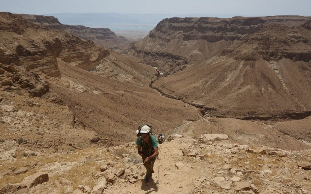 Dans le désert de Judée, un bénévole utilise une corde pour descendre dans une grotte du Canyon Tzeelim, au-dessus de la mer Morte (au fond), le 1er juin 2016. (Crédit : AFP PHOTO/MENAHEM KAHANA)