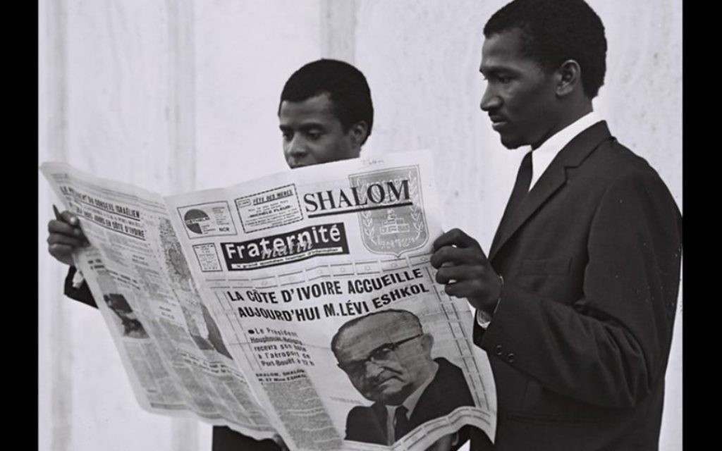 Des habitants de Côte d'Ivoire lisent un journal annonçant la visite du Premier ministre Levi Eshkol dans le pays, le 31 mai 1966. (Crédit : Moshe Fridan/GPO)