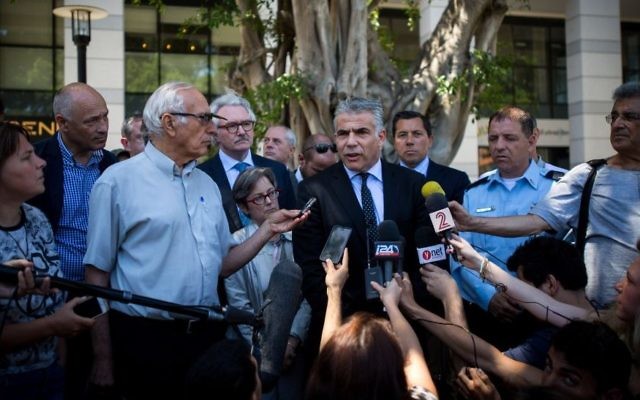 Le leader de Yesh Atid Yair Lapid parle à la presse, entouré de diplomates étrangers après avoir visité le restaurant Max Brenner, le site d'une attaque terroriste le 8 juin au marché de Sarona, Tel Aviv, le 10 juin, 2016. (Crédit : Miriam Alster / Flash90)