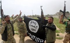 Des membres de l'unité paramilitaire irakienne Mobilisation Populaire célèbrent la reprise du village d'Albu Ajil, près de la ville de Tikrit, qui était détenu par l'Etat islamique, en agitant un drapeau du groupe terroriste, le 9 mars 2015 (Crédit : AFP/Ahmad al-Rubaye)