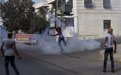 Un jeune Palestinien masqué renvoie des gaz lacrymogènes sur les garde-frontières israéliens pendant des affrontements dans le village palestinien d'al-Ram, entre Jérusalem et Ramallah, en Cisjordanie, le 22 octobre 2015. (Crédit : AFP/Abbas Momani)