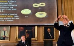 Thors Hans Hansson (à droite), membre du Comité Nobel pour la physique, utilise un bretzel pour illustrer ses explications lors d'une conférence de presse pour annoncer les gagnants du Prix Nobel de physique 2016 à l'Académie royale suédoise des sciences à Stockholm, en Suède, le 4 octobre 2016 (Crédit : AFP PHOTO / TT AGENCE DE NOUVELLES / Anders WIKLUND / Suède OUT)