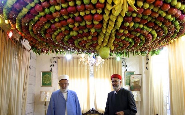 Le grand prêtre Samaritain, Abdullah Wassef Tawfiq, se tient avec son frère Husney Cohen dans son salon avec une « succah » fait maison à base de fruits frais pour la fête des Tabernacles ou Souccot, sur le mont Garizim près de la ville de Naplouse en Cisjordanie , le 18 Octobre, 2016 (Crédit : Dov Lieber / Times of Israel)