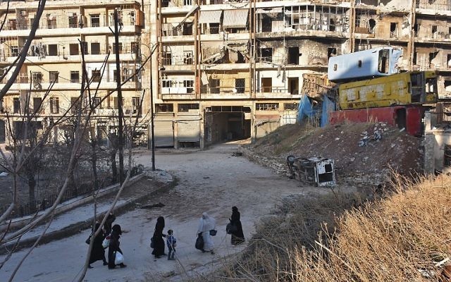 Des Syriens fuyant les violences dans les quartiers est d'Alep, tenus par les rebelles, passent devant une barricade improvisée de carcasses de bus dans le quartier Bal al-Hadid, saisi par les forces du régime gouvernemental, le 7 décembre 2016. (Crédit : George Ourfalian/AFP)