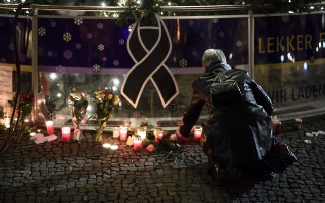 Une femme allume une bougie sous un arbre de Noël à proximité de la porte de Brandenburg à Berlin le 20 décembre 2016, un jour après qu'un camion-bélier ait fondé sur un marché de Noël. (Crédit : Clemens Bilan/AFP)