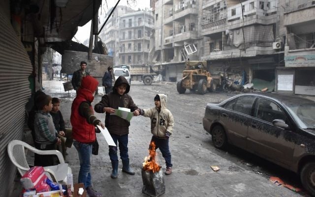 Des enfants syriens rassemblés autour d'un feu dans les rues d'Alep, pendant l'offensive gouvernementale pour reprendre la ville, le 27 décembre 2016. (Crédit : George Ourfalian/AFP)