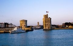 L' avant port de La Rochelle un soir de coucher de soleil doré au mois de mai. A droite, la Tour Saint-Nicolas, à l' arrière plan le clocher de l' église Saint-Sauveur, à gauche, la Tour de la Chaîne. Plus en avant, "L'Ilienne" (1973, IMO 7336185) amarré au ponton d' embarquement des "Croisières Inter-Îles", entreprise de tourisme qui organise des excursions et des promenades en mer vers les îles avoisinantes. La Rochelle, Charente Maritime, France (Crédit : Jpbazard/CC BY SA 3.0)