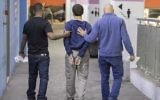 L'adolescent juif israélo-américain, (au centre), qui a été accusé d'avoir lancé des dizaines d'alertes à la bombe antisémites aux Etats-Unis et ailleurs, escorté par des gardes alors qu'il quitte le tribunal de Rishon Lezion, le 23 mars 2017. (Crédit : Jack Guez/AFP)