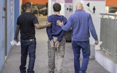 L'adolescent juif israélo-américain, (au centre), qui a été accusé d'avoir lancé des dizaines d'alertes à la bombe antisémites aux Etats-Unis et ailleurs, escorté par des gardes alors qu'il quitte le tribunal de Rishon Lezion, le 23 mars 2017. (Crédit : Jack Guez/AFP)