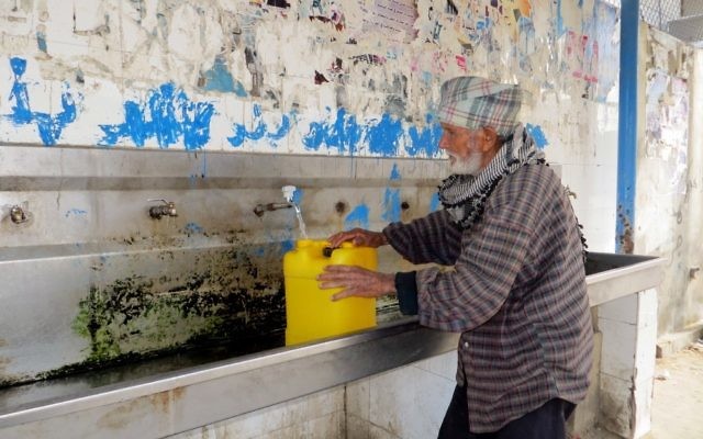 Un homme âgé remplit un bidon d'eau à un robinet à l'usine de traitement des eaux usées de l'autorité de l'Eau à Khan Yunis (Crédit : CC-BY-4.0 Muhammad Sabah B'Tselem / Wikipedia)