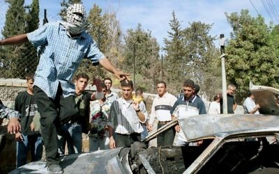 Un Palestinien célébrant sur le toit d'une voiture brûlée le lynchage de deux réservistes israéliens, à Ramallah, le 12 octobre 2000. (Crédit : Flash90)