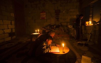 Une Palestinienne aide son fils à faire ses devoirs à la lumière des bougies, alors qu'une crise électrique touche la bande de Gaza, dans le camp de réfugiés de Khan Yunis, le 19 avril 2017. (Crédit : Mahmud Hams/AFP)