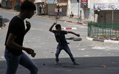 Illustration : Des manifestants palestiniens jettent des pierres sur des soldats israéliens à Hébron, en Cisjordanie, le 27 avril 2017.. (Crédit : Hazem Bader/AFP)