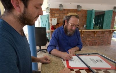 Le rabbin Aaron Leibowitz, au centre, fondateur de Hashgach Pratit (Supervision privée en hébreu), signe un certificat de casheroute alternatif à celui du grand rabbinat pour un bar du centre de Jérusalem, le 8 juin 2016. (Crédit : Menahem Kahana/AFP)