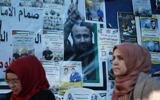Des Palestiniennes devant un mur d'affiches, dont un portrait de Marwan Barghouthi, pendant un rassemblement de soutien aux prisonniers palestiniens en grève de la faim, à Ramallah, en Cisjordanie, le 24 avril 2017. (Crédit : Abbas Momani/AFP)
