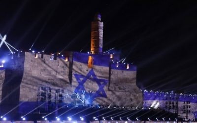 Les gens regardent une projection du drapeau israélien au cours d'un spectacle de son et lumière projeté sur les murs de la Vieille ville de Jérusalem pour célébrer le début de la semaine du 50ème anniversaire de la guerre israélo-arabe de 1967, le 20 mai 2017 (Crédit : GALI TIBBON / AFP PHOTO)