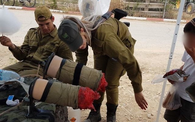 Des soldats de la brigade Etzion montrent une paire de fausses jambes amputées à un enfant de l'implantation de Tekoa pendant une exposition militaire pour Yom HaAtsmaout, le 2 mai 2017. (Crédit : autorisation) Des soldats de la brigade Etzion montrent une paire de fausses jambes amputées à un enfant de l'implantation de Tekoa pendant une exposition militaire pour Yom HaAtsmaout, le 2 mai 2017. (Crédit : autorisation)