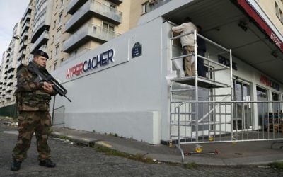 Un soldat français monte la garde alors qu'un employé municipal pose une plaque commémorative devant le supermarché juif Hyper Cacher à Paris, le 4 janvier 2016, en mémoire des quatre personnes tuées durant un attentat terroriste dans le magasin le 9 janvier 2015. (Crédit : Thomas Samson/AFP)