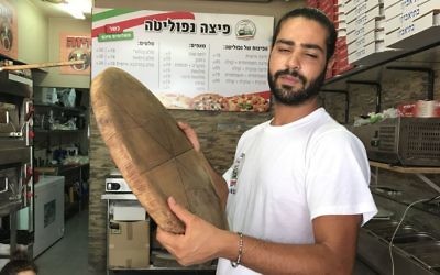 Shlomi Madar avec un plateau à pizza en bois, similaire à celui qu'il a employé pour neutraliser un terroriste palestinien qui a tenté de le poignarder dans sa pizzeria, à Petah Tikva, le 24 juillet 2017. (Crédit : Jacob Magid)