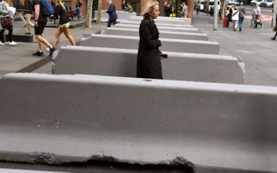 Les piétons passent à côté des bornes de sécurité en béton installées près du Lindt Cafe, où un homme a pris en otage des clients en 2014,  le 17 juillet 2017 (Crédit : AFP / WILLIAM WEST)