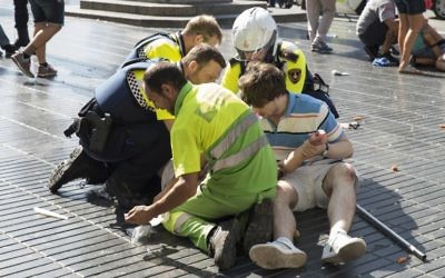 Des policiers et deux hommes viennent en aide à une victime après un attentat au cours duquel le conducteur d'une fourgonnette a dirigé son véhicule dans la foule, tuant au moins 13 personnes et faisant environ 100 blessés à la Rambla, à Barcelone, le 17 août 2017 (Crédit : Nicolas CARVALHO OCHOA/AFP PHOTO)