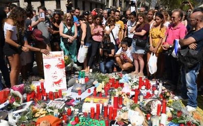 Des gens se recueillent auprès des fleurs, des bougies et autres objets posés sur le boulevard Las Ramblas à Barcelone alors qu'ils rendent hommage aux victimes de l'attentat de Barcelone le 18 août 2017. (Crédit : PASCAL GUYOT/AFP)